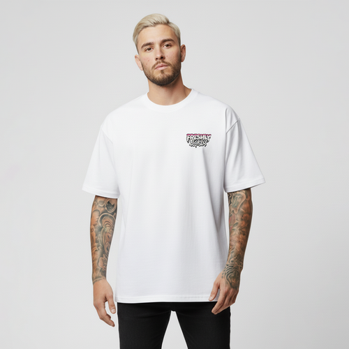 A man with blonde hair and tattoos wearing a white short-sleeve t-shirt with a small graphic on the left chest, paired with black pants, against a light gray background.