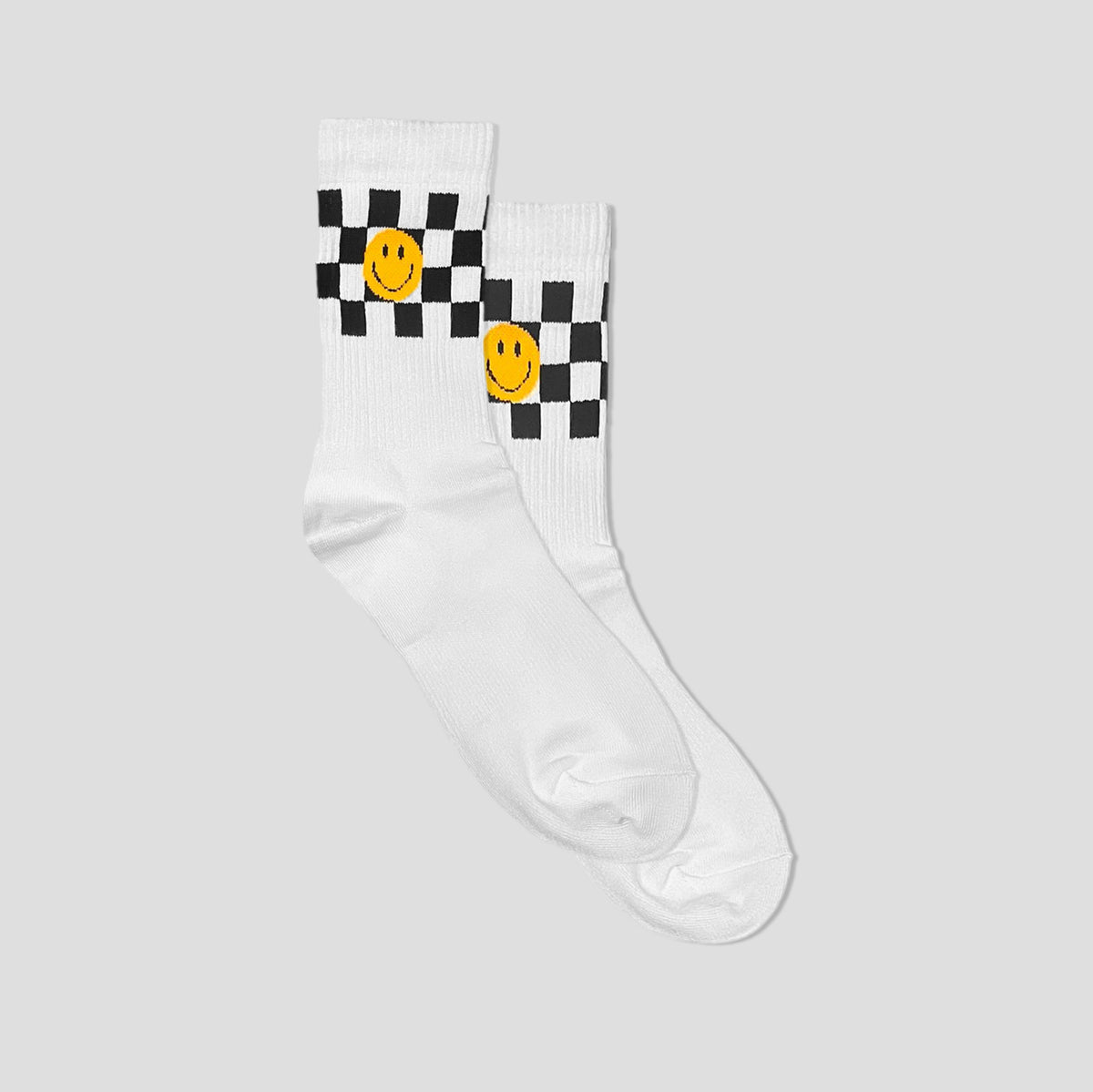 A pair of white crew socks with a black and white checkerboard pattern and a yellow smiley face on each cuff, shown against a solid light gray background.