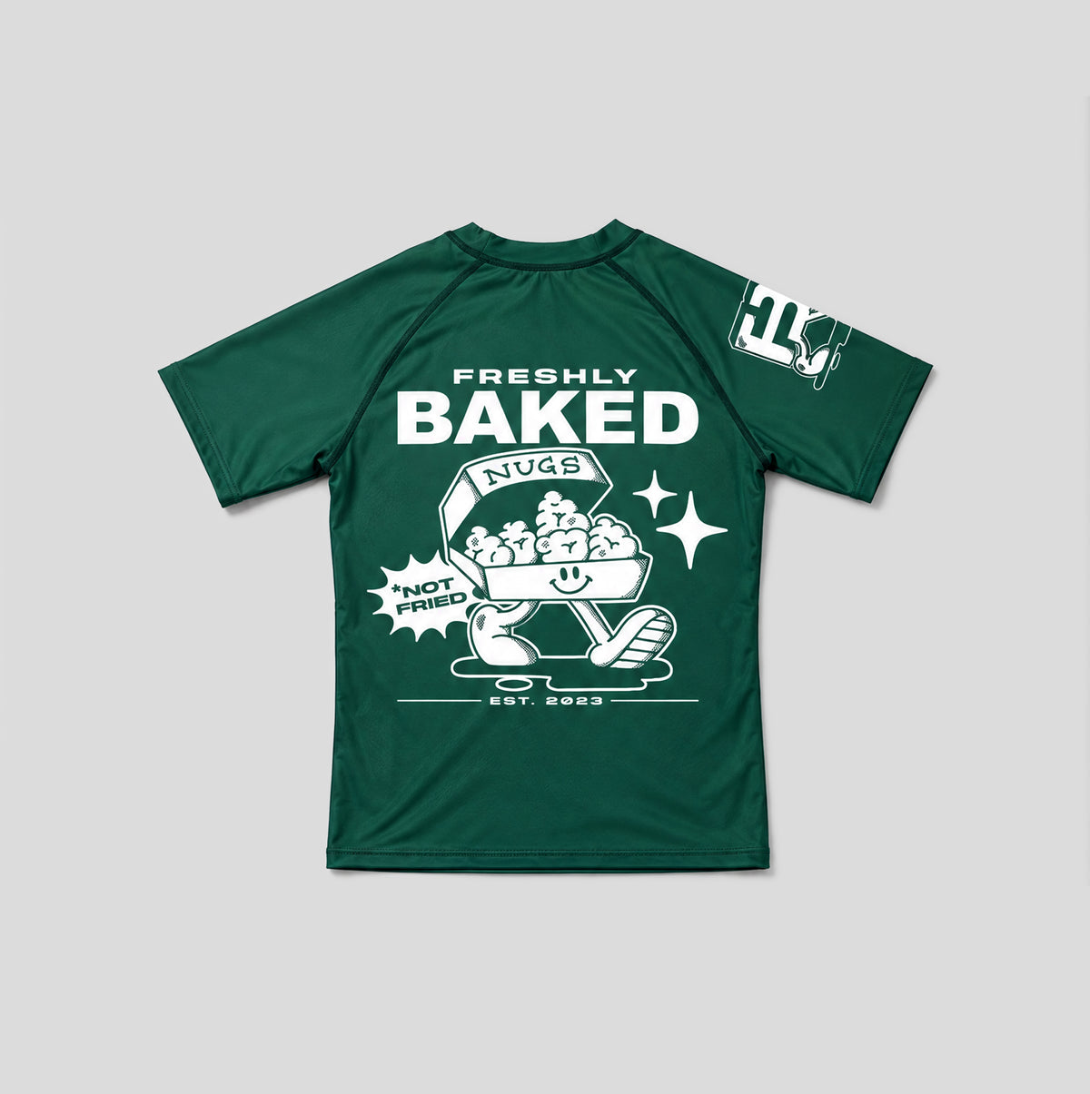 A dark green short-sleeve t-shirt with a white graphic print on the front reading 'FRESHLY BAKED NUGS' and 'HOT DUTCH', alongside a cartoon bagel character. A smaller white graphic is visible on the right sleeve.