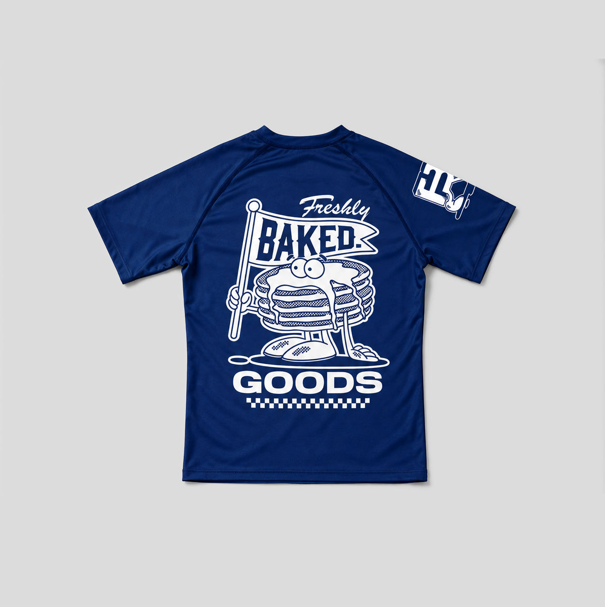 A navy blue short-sleeve athletic t-shirt shown from the back, featuring a large white graphic print of a stack of pancakes with a face holding a sign that reads 'Freshly Baked GOODS'. A smaller white graphic is visible on the left sleeve.