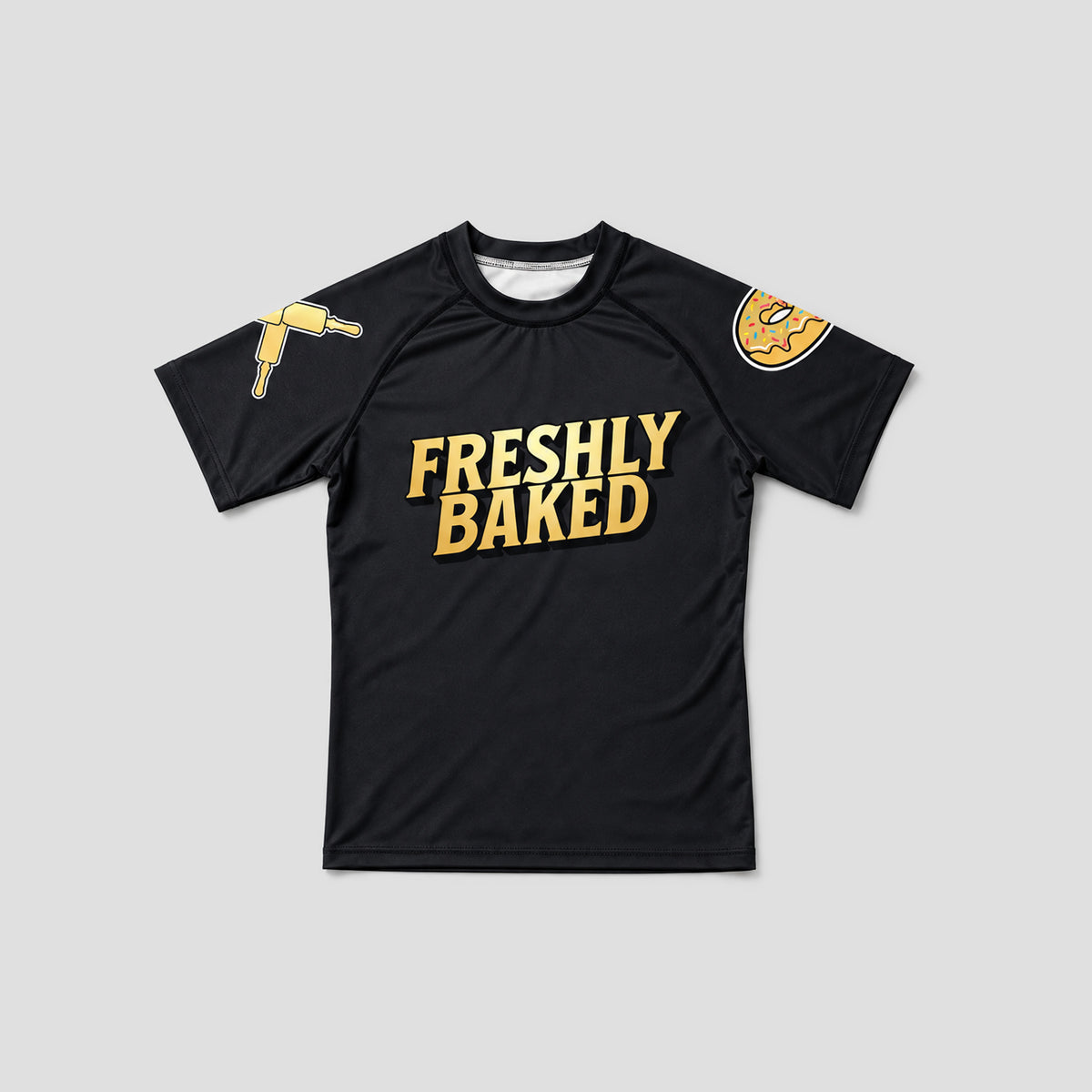 A black short-sleeve athletic t-shirt with 'FRESHLY BAKED' printed in bold gold letters across the chest. The left sleeve features a gold hot air balloon graphic, and the right sleeve features a gold donut graphic.