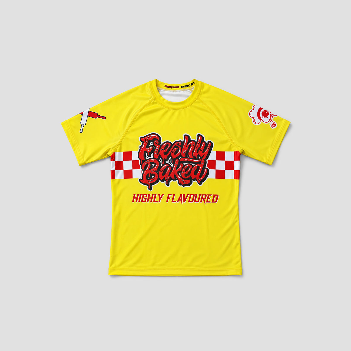 A bright yellow short-sleeve t-shirt with a red and white checkered stripe across the chest, featuring the text 'Foodily Baked' in red and black script, and 'HIGHLY FLAVOURED' printed below. The shirt is displayed flat against a light gray background.