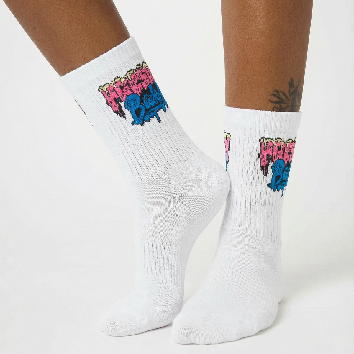 White crew socks worn on a person's feet, featuring a colorful graffiti-style graphic with pink, blue, and yellow elements near the cuff.