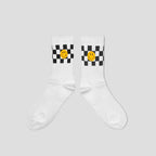 A pair of white crew socks with a black and white checkered pattern and a yellow smiley face graphic on the upper calf, displayed against a solid light gray background.