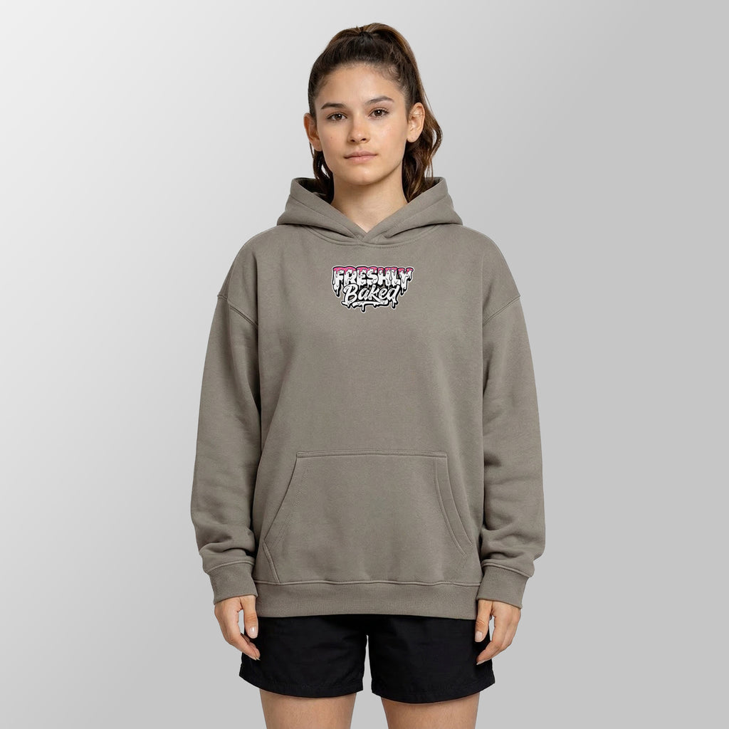 A woman modeling a taupe gray pullover hoodie with a 'Freshly Baked!' graphic on the chest, paired with black shorts, against a neutral gray background.