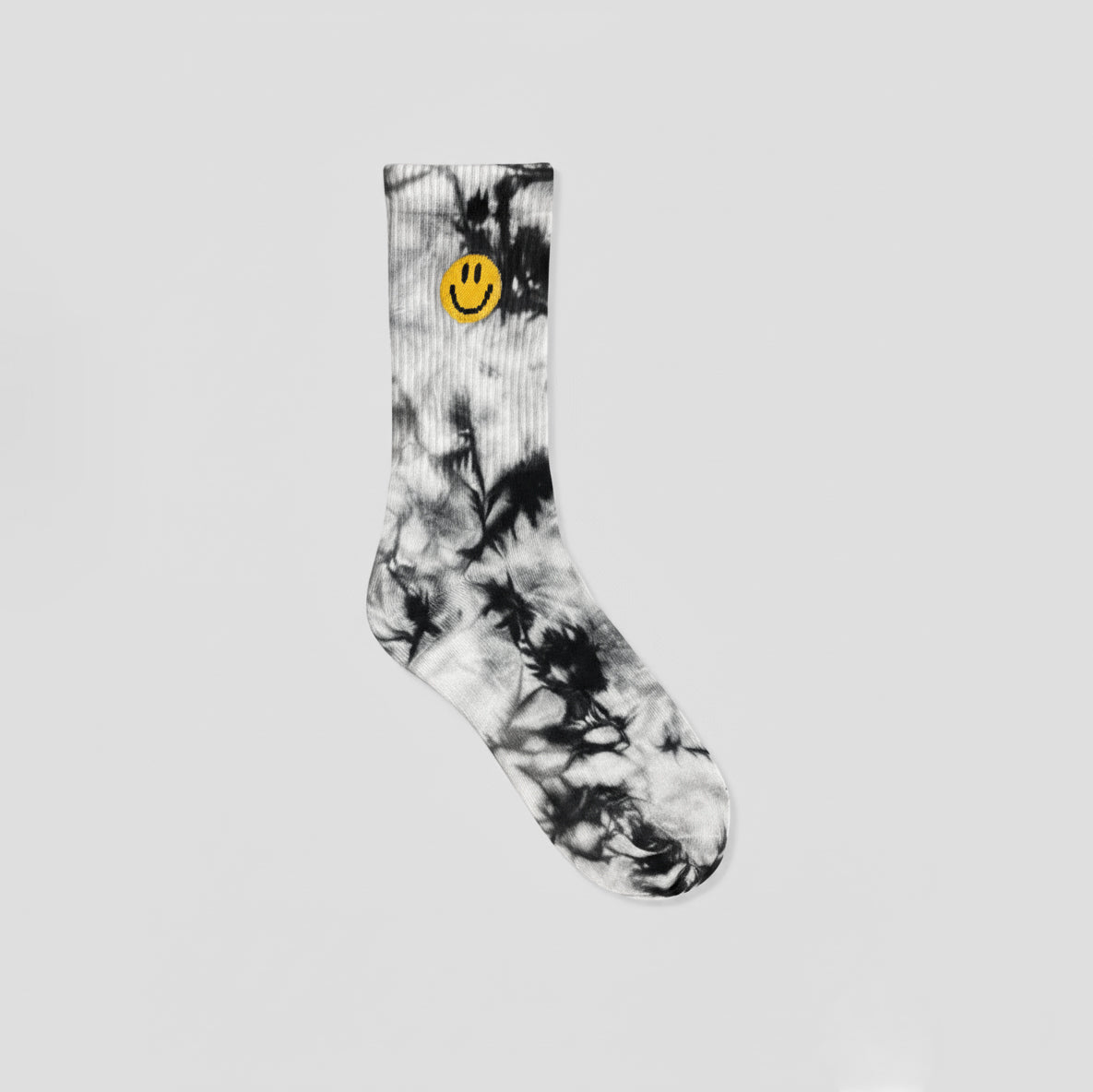A single crew sock with a black and white tie-dye pattern and a yellow smiley face logo near the cuff, shown against a solid light gray background.