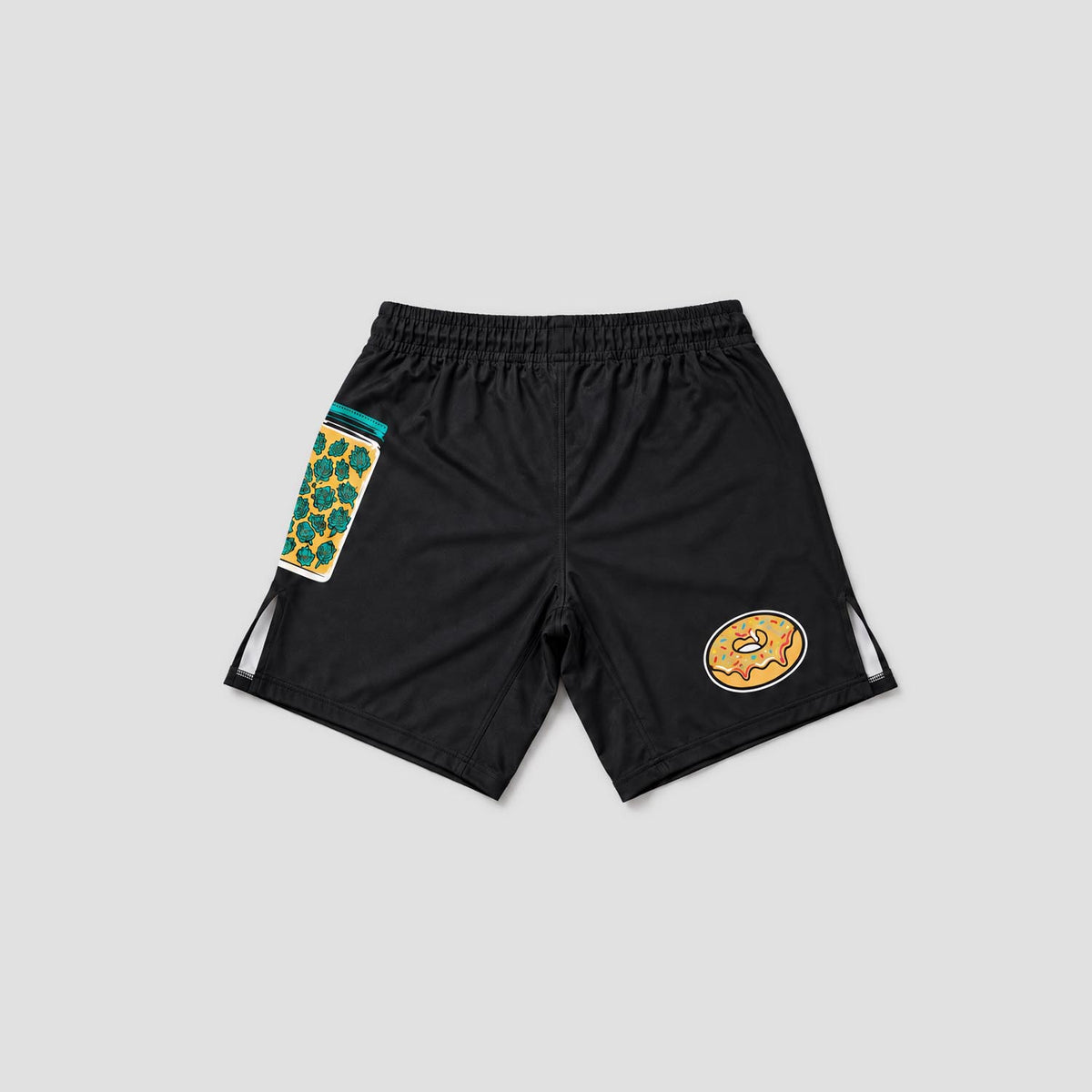 Black athletic shorts with a patterned green and yellow patch on the left leg, a cartoon donut graphic on the right leg, and white side cutouts, shown on a light gray background.