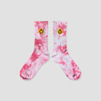 A pair of pink and white tie-dye crew socks with a small yellow smiley face embroidered on the ribbed cuffs, displayed against a solid light gray background.