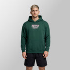 A man wearing a dark green pullover hoodie with a 'Freshly Baked' graphic on the chest, paired with black athletic shorts, standing against a light gray studio background.