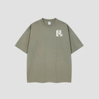 An oversized short-sleeve t-shirt in a muted sage green color, featuring a white graphic logo on the left chest, displayed against a neutral light gray background.