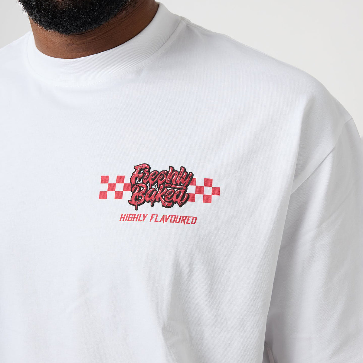 A close-up of a person wearing a white long-sleeve t-shirt with a red and black graphic on the chest that reads 'Breathe Baked' and 'HIGHLY FLAVOURED' underneath.