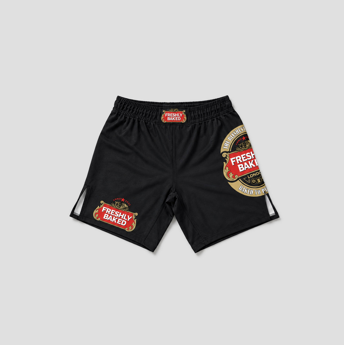 Black athletic shorts featuring 'Freshly Baked' brand graphics, including a large circular logo on the left leg and a smaller rectangular patch on the right leg, displayed against a light gray background.