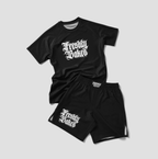 A two-piece athletic set consisting of a black short-sleeve t-shirt and matching black shorts, both featuring the text 'Freshly Baked' in a white gothic font. The t-shirt has a larger graphic on the chest, while the shorts feature a smaller version on the left leg.