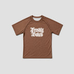 A brown short-sleeve athletic t-shirt with a white gothic-style 'Freshly Baked' graphic printed on the chest, displayed flat against a light gray background.