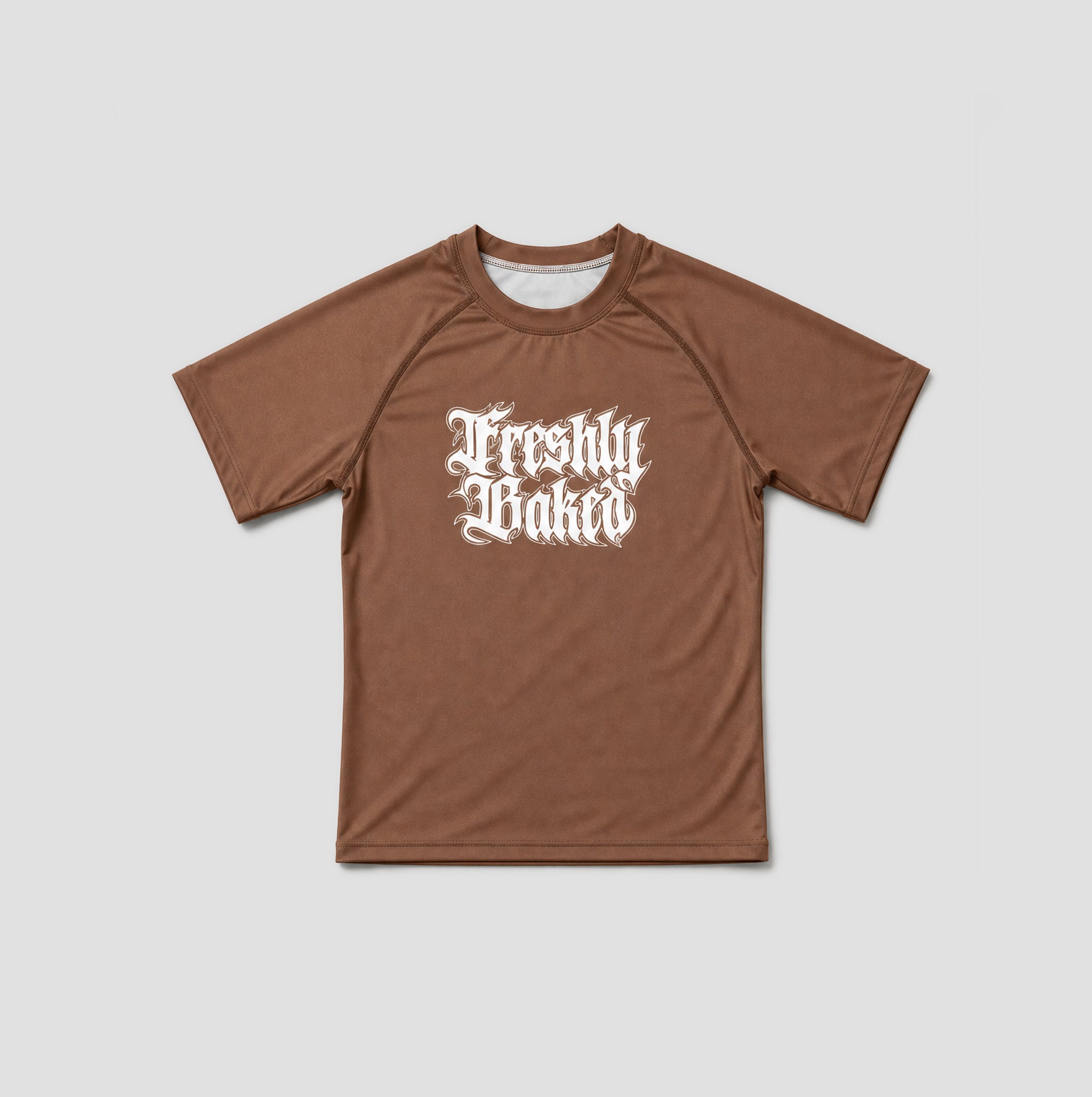 A brown short-sleeve athletic t-shirt with a white gothic-style 'Freshly Baked' graphic printed on the chest, displayed flat against a light gray background.