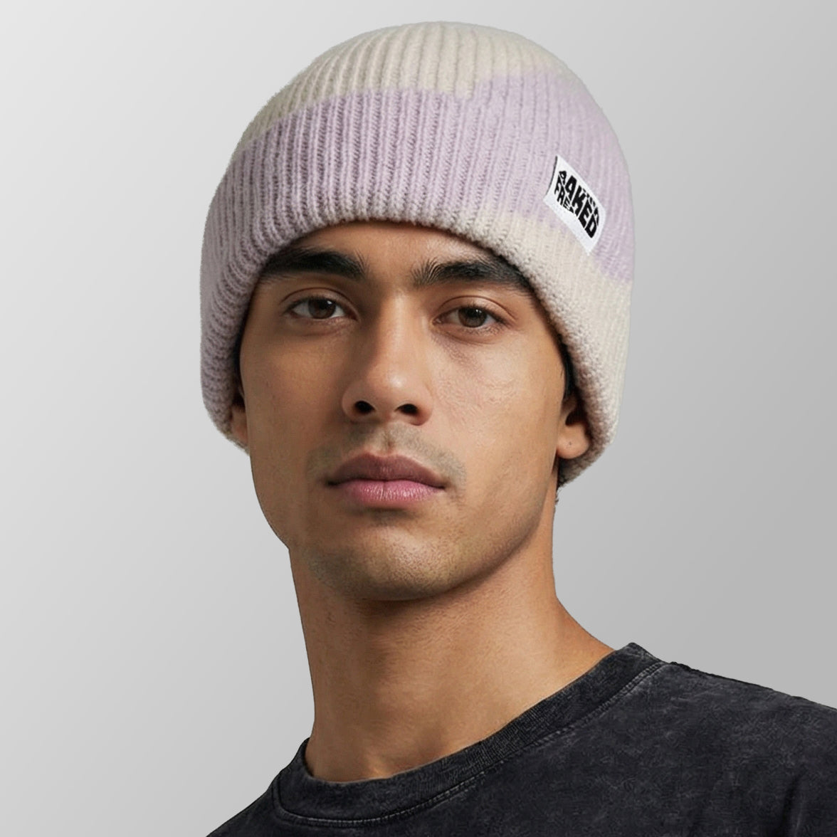 A man wearing a ribbed knit beanie hat with horizontal stripes in cream, light purple, and pale pink, featuring a small black and white FRESHLY BAKED logo patch on the side, against a neutral gray background.