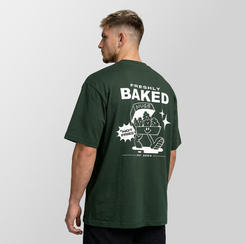 A man wearing a dark green t-shirt, viewed from the back. The shirt features a large white graphic print on the back with the text 'FRESHLY BAKED NUGS' and 'NOT FRIED EST 2023.