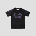 A black short-sleeve raglan t-shirt with 'Freshly Baked' printed in a purple gothic font on the chest, featuring purple gothic patterns on the shoulders, shown against a light gray background.