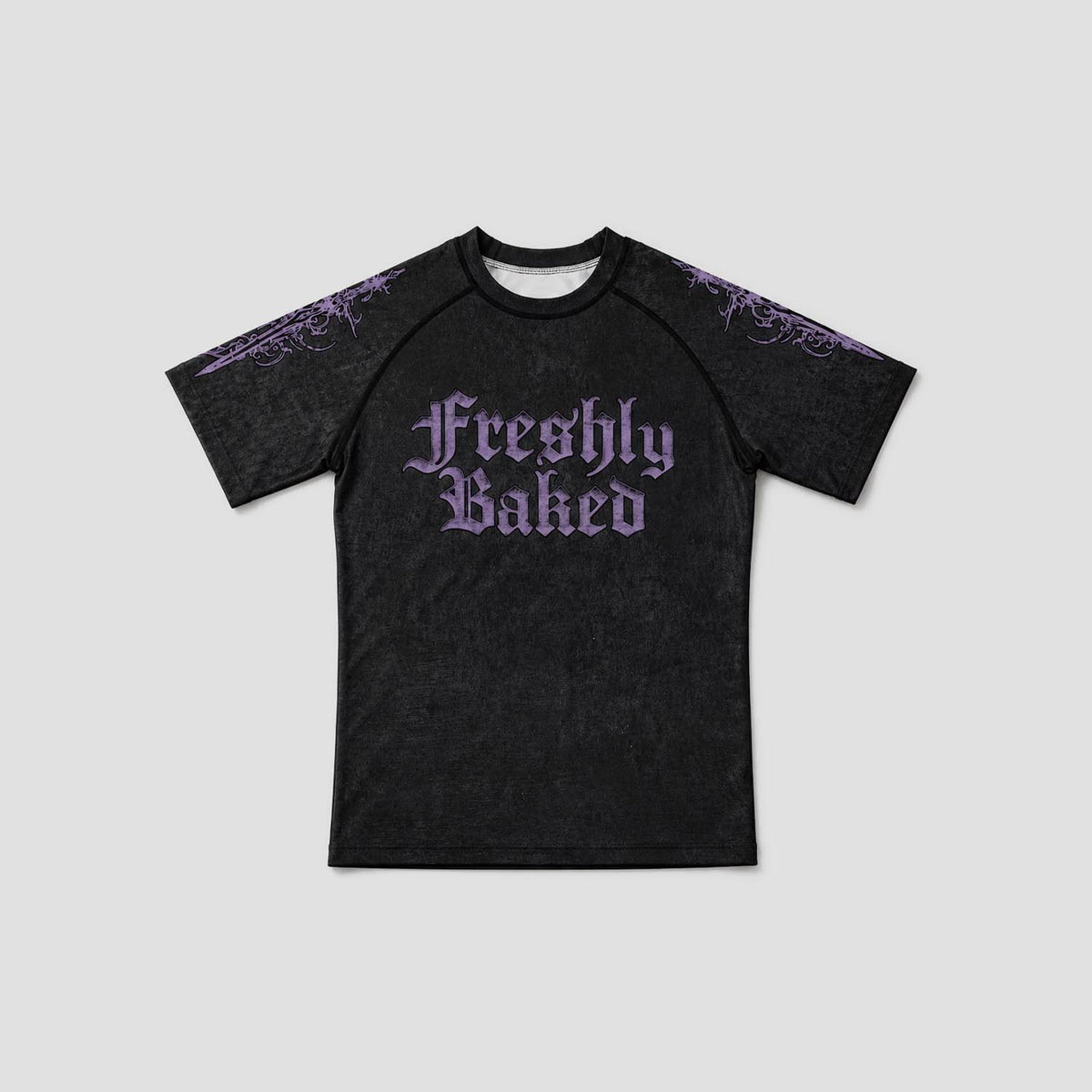 A black short-sleeve raglan t-shirt with 'Freshly Baked' printed in a purple gothic font on the chest, featuring purple gothic patterns on the shoulders, shown against a light gray background.