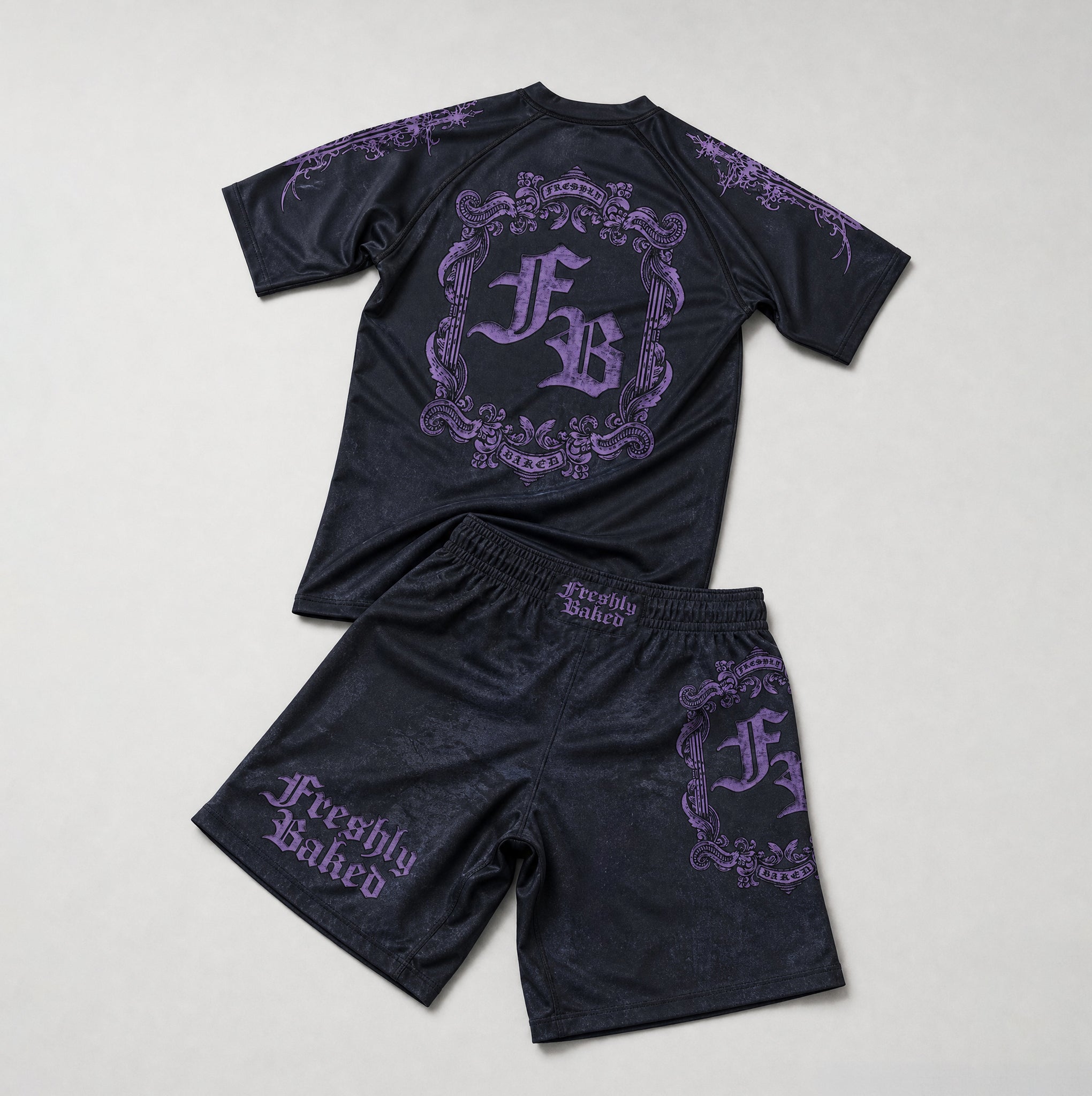 A two-piece swimwear set consisting of a short-sleeve rash guard and matching shorts in black with purple gothic-style lettering and ornate crest graphics, laid flat on a light gray background.