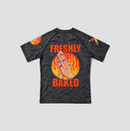 A dark gray acid-wash short-sleeve t-shirt with a graphic on the back featuring a hand with rings, flames, and the text 'FRESHLY BAKED' in orange, shown on a light gray background.