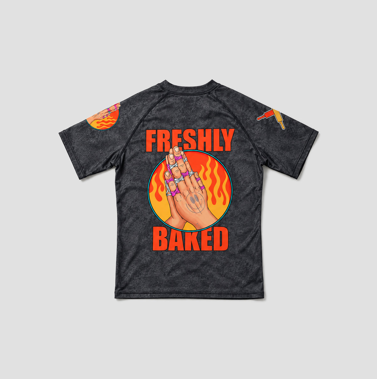 A dark gray acid-wash short-sleeve t-shirt with a graphic on the back featuring a hand with rings, flames, and the text 'FRESHLY BAKED' in orange, shown on a light gray background.