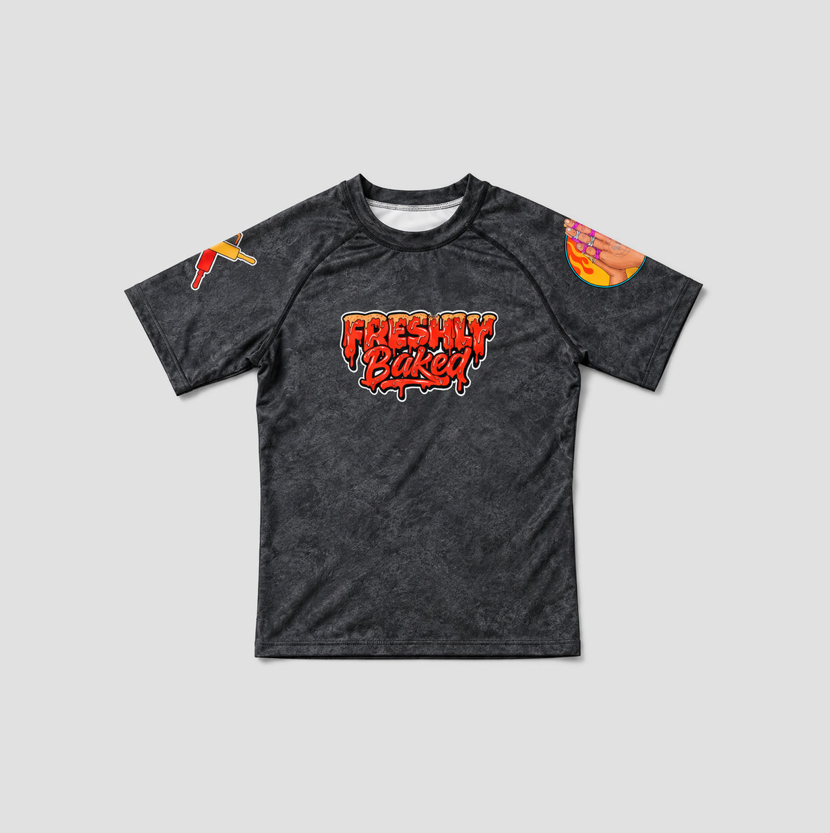 A dark gray heathered short-sleeve t-shirt with a 'Freshly Baked' graphic in red and orange on the chest, featuring a small red and yellow graphic on the right sleeve and a larger orange and yellow graphic on the left sleeve, displayed against a light gray background.