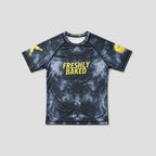 A short-sleeve athletic t-shirt with a dark gray and black mottled pattern, featuring the words 'FRESHLY BAKED' in yellow on the chest, a gold donut face on the right sleeve, and a gold graphic on the left sleeve, displayed against a light gray background.