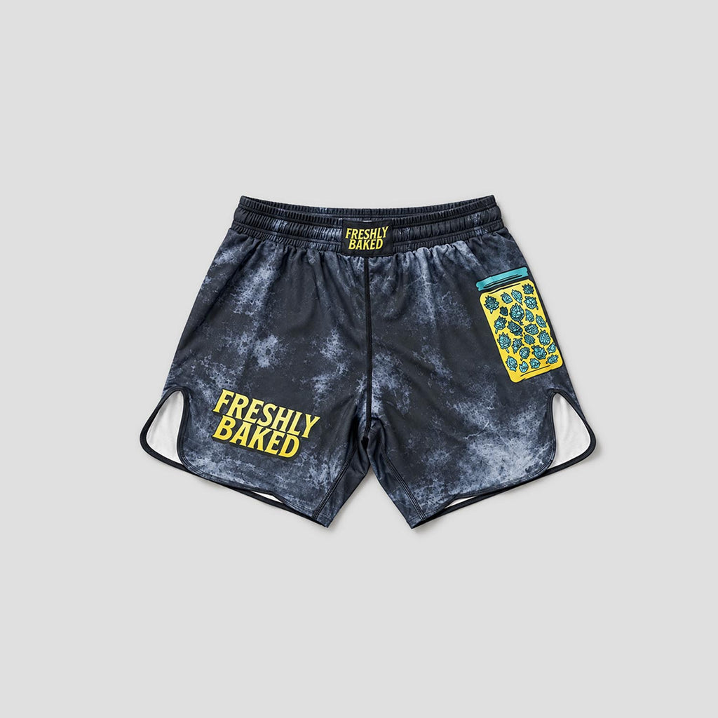 A pair of athletic shorts with a dark gray and white marble pattern, featuring 'FRESHLY BAKED' printed in yellow on the left leg and a yellow and blue patterned patch on the right leg.