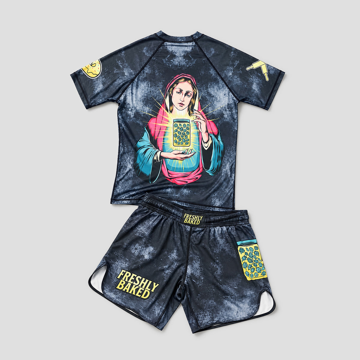 A two-piece unisex athletic set consisting of a short-sleeve rash guard and matching shorts, featuring a dark blue/black mottled tie-dye pattern. The rash guard has a large graphic of a woman holding a playing card on the front, with a yellow playing card patch on the sleeve.