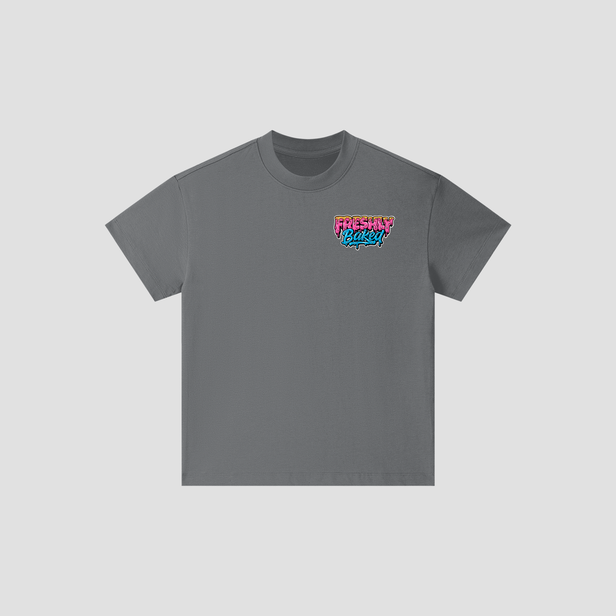 A dark gray crewneck t-shirt with a colorful graphic on the left chest reading 'FRESHLY BAKED' in pink and blue, displayed on a light gray background.