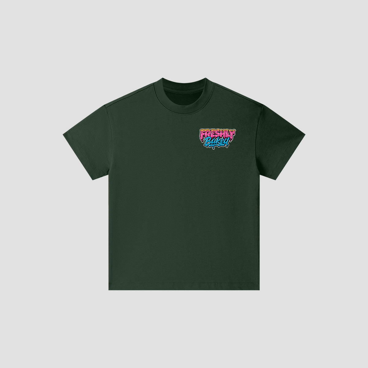 A dark forest green short-sleeve crewneck t-shirt with a colorful retro-style graphic on the left chest reading 'Freshly Baked' in pink, blue, and white, displayed on a light gray background.