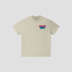 A light beige crewneck t-shirt with a colorful graphic on the left chest reading 'FRESHLY BAKED' in pink, blue, and green, displayed on a neutral light gray background.