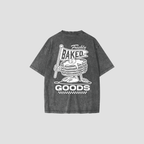 A dark gray acid-wash t-shirt shown from the back, featuring a white graphic print of a stack of pancakes with a flag that reads 'Freshly Baked' and the words 'GOODS' below.