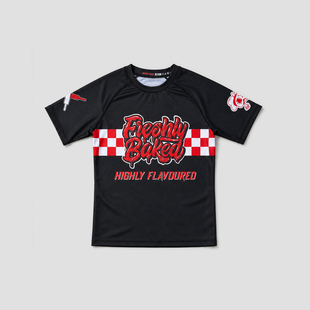 A black short-sleeve athletic t-shirt with a red and white checkered graphic across the chest reading 'Freshly Baked' and 'HIGHLY FLAVOURED' in red. The shirt features a small red and white logo on the right sleeve and a small white graphic on the left sleeve, displayed against a solid light gray background.