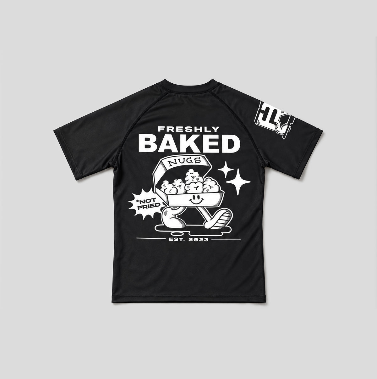 A black short-sleeve t-shirt with a white graphic print on the front and sleeve, featuring the text 'FRESHLY BAKED' and a cartoon character with a basket of cookies.