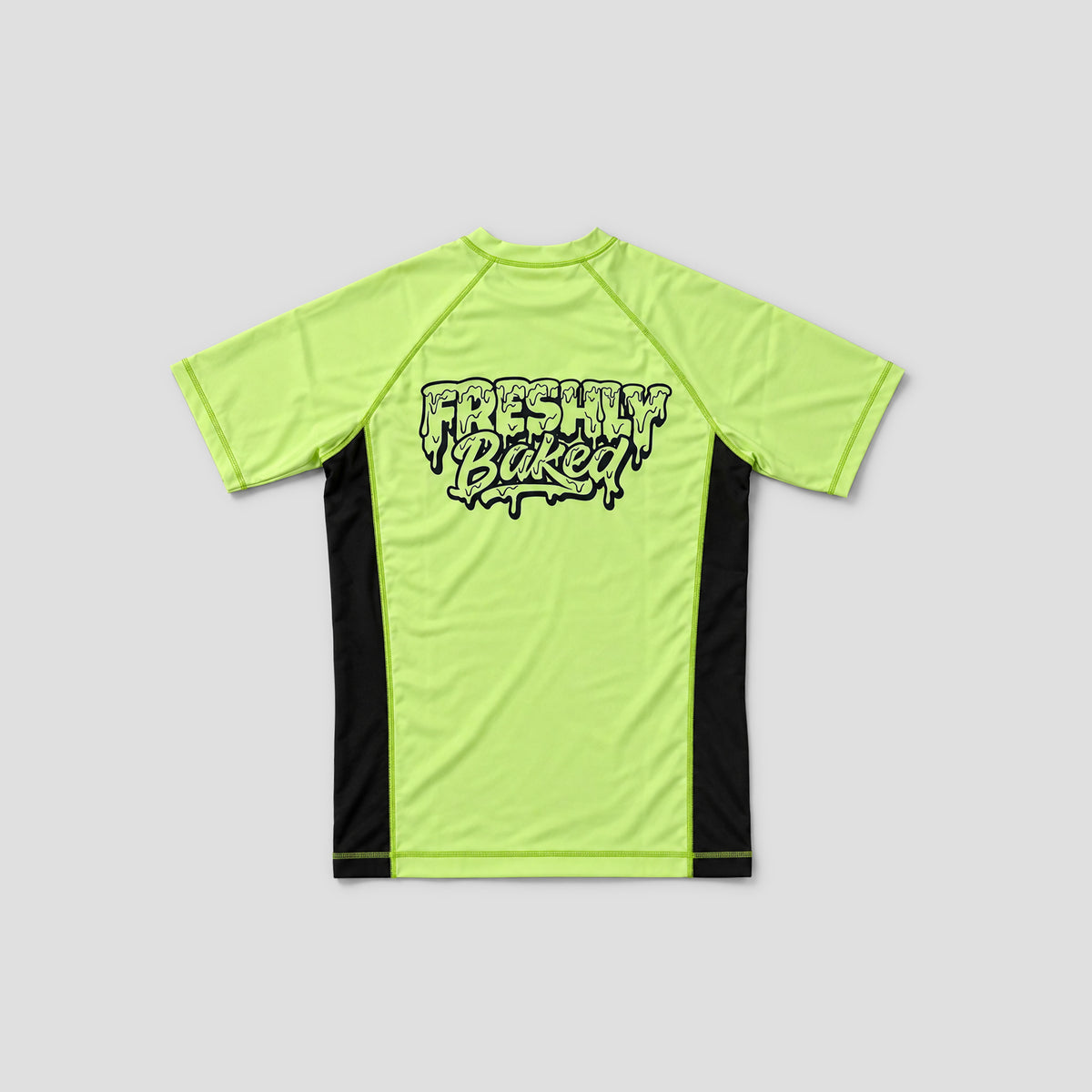 A short-sleeve athletic jersey shown from the back, featuring a bright neon yellow-green body with black side panels and a black graphic text print reading 'Freshly Baked' across the upper back, set against a solid light gray background.