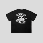 A black short-sleeve t-shirt with a white graphic print on the front, featuring the text 'FRESHLY BAKED' and a cartoon character holding a bowl of cookies, set against a solid gray background.