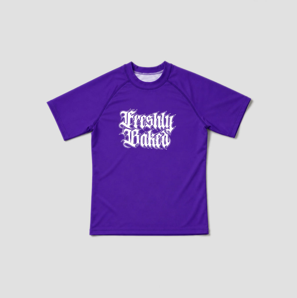 A purple short-sleeve crewneck t-shirt with 'Freshly Baked' printed in a white gothic font on the chest, displayed against a light gray background.