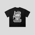 A black short-sleeve t-shirt with a white graphic print on the front. The graphic features a cartoon stack of pancakes holding a flag that says 'Freshly BAKED GOODS'.