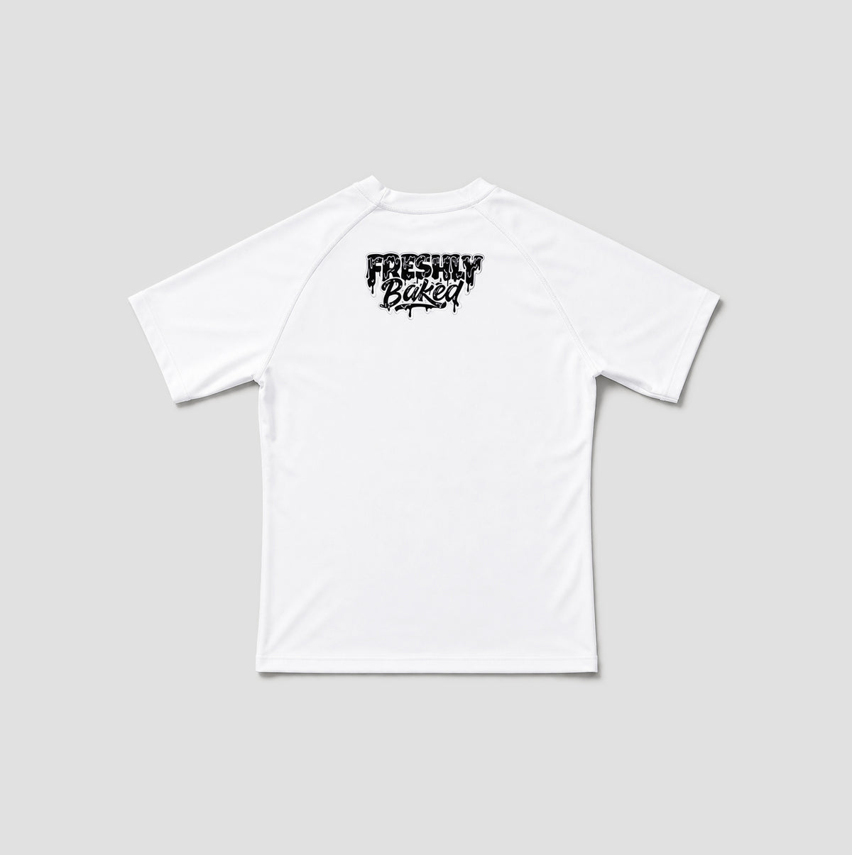 A white short-sleeve t-shirt shown from the back, featuring a black distressed graphic print that reads 'FRESHLY BAKED' across the upper back, set against a solid light gray background.