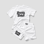 A white athletic two-piece set consisting of a short-sleeve raglan t-shirt and matching shorts, both featuring a black gothic-style 'Freshly Baked' graphic. The t-shirt is laid flat on top of the shorts against a neutral light gray background.