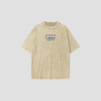 A light beige acid-wash t-shirt with a 'Freshly Baked' graphic on the chest, displayed against a solid light gray background.