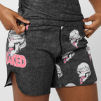 Close-up of a person wearing dark gray heathered shorts with a repeating skull-and-mouth graphic and large pink 'BAKED' text on the left leg, shown against a light gray studio background.