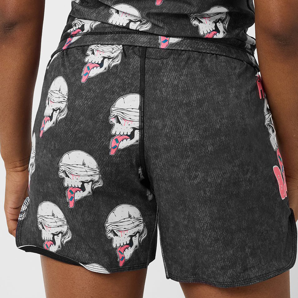 Close-up of a person wearing dark charcoal gray athletic shorts with an allover graphic print of white skulls with pink and red tongues sticking out.