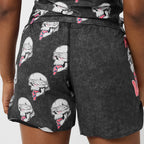 Close-up of a person wearing dark charcoal gray athletic shorts with an allover graphic print of white skulls with pink and red tongues sticking out.