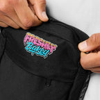 Close-up of a black fabric bag being held open by two hands, showing a colorful embroidered logo that reads 'Freshly Baked' in pink, yellow, blue, and white.