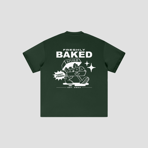 A dark forest green t-shirt with a white graphic print on the front, featuring a cartoon character hugging a basket of cookies and the text 'FRESHLY BAKED' and 'NOT FRIED EST. 2023'.