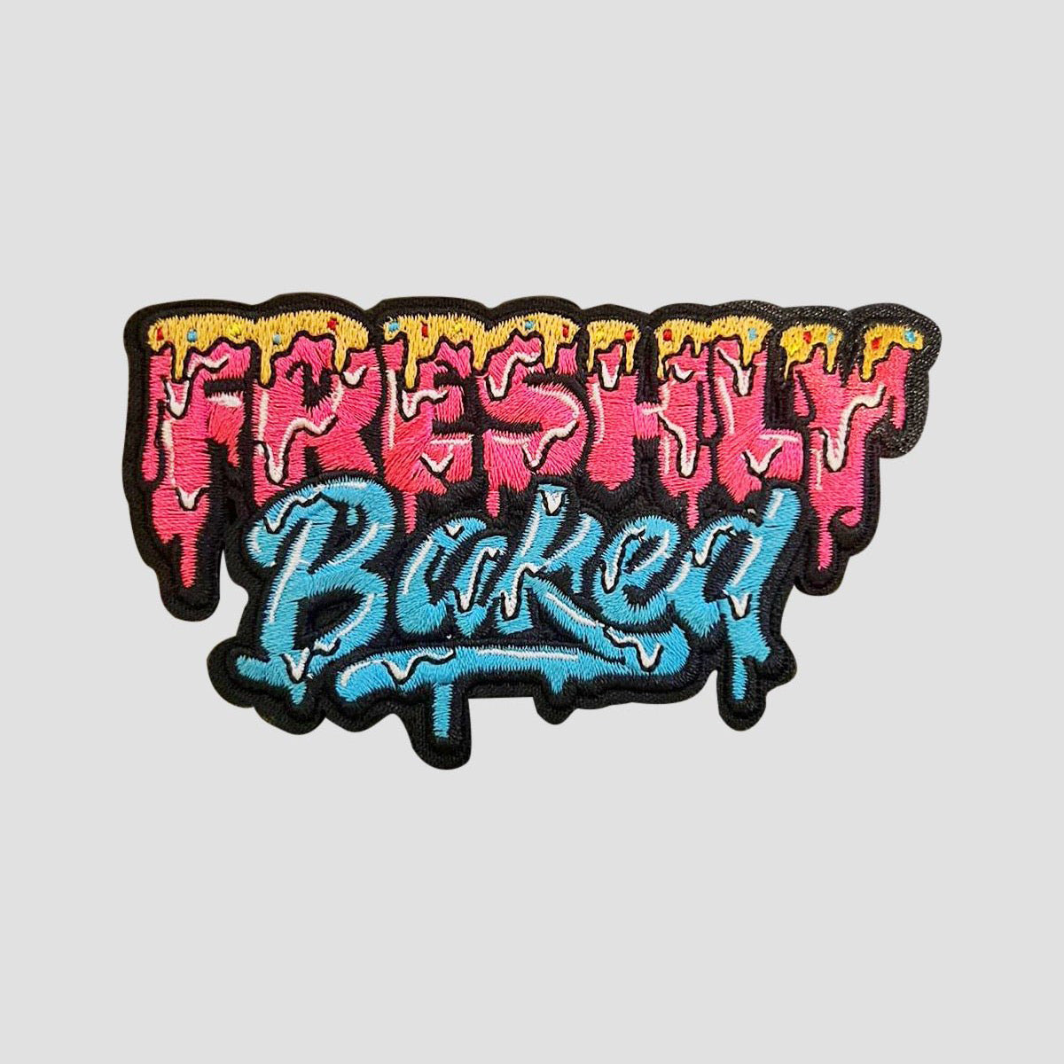 An embroidered patch with the text 'Freshly Baked' in a dripping graffiti style. The top portion reads 'Freshly' in pink with yellow dripping details, and the bottom portion reads 'Baked' in blue with white dripping details.