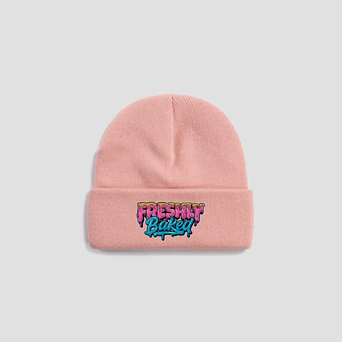 A light pink knit beanie hat with a folded cuff featuring a colorful 'Freshly Baked' graffiti-style embroidered logo, shown against a solid light gray background.